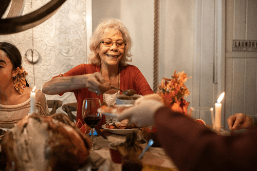 An elegant senior woman in a rust cardigan enjoys a heartwarming bowl of soup at a beautifully set dining table, highlighting the essence of nutrition and dietary support in senior care.