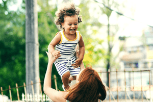 A joyful toddler being lifted into the air by a woman, illustrating a moment of carefree play.