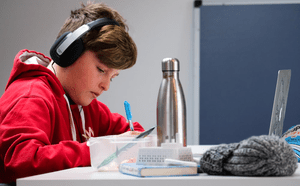 A focused young boy studying independently with headphones on.