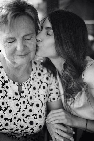 A greyscale photo of a female kissing an elderly woman on her cheek.