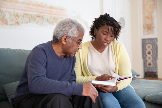 A woman reading a book while sitting beside a senior man in a blue sweater. 