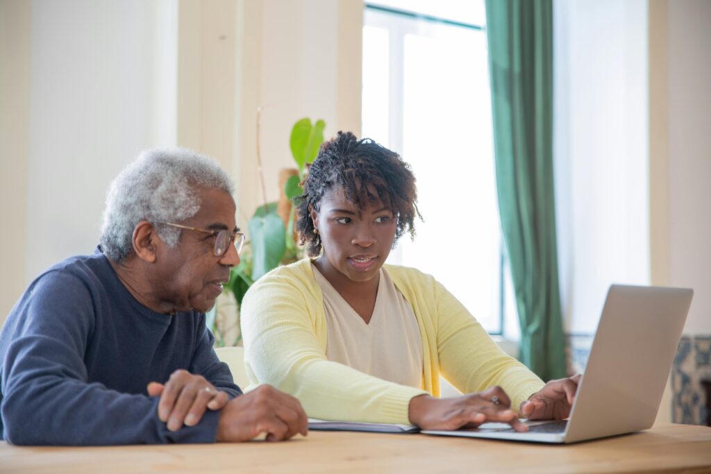 Support worker talking with and assisting an elderly man using a laptop