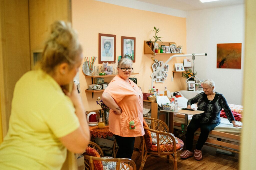 Elderly woman receiving assistance from support workers in a nursing home setting