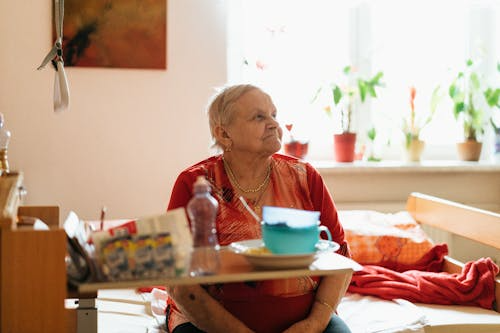 Elderly woman sitting on a bed with a table of food in a care setting