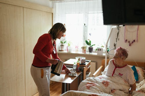 Support worker serving tea to an elderly woman in a nursing home setting