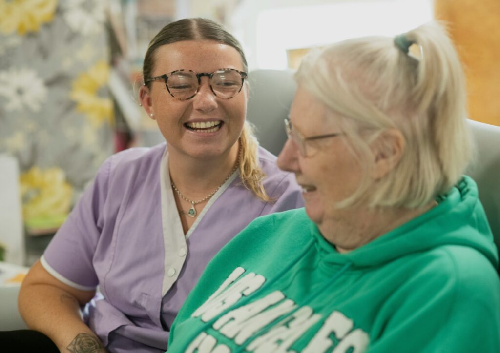 support worker smiling and talking with an elderly resident in a relaxed care environment