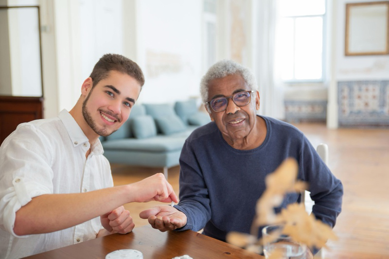 Professional support worker providing companionship to an elderly individual in a living room