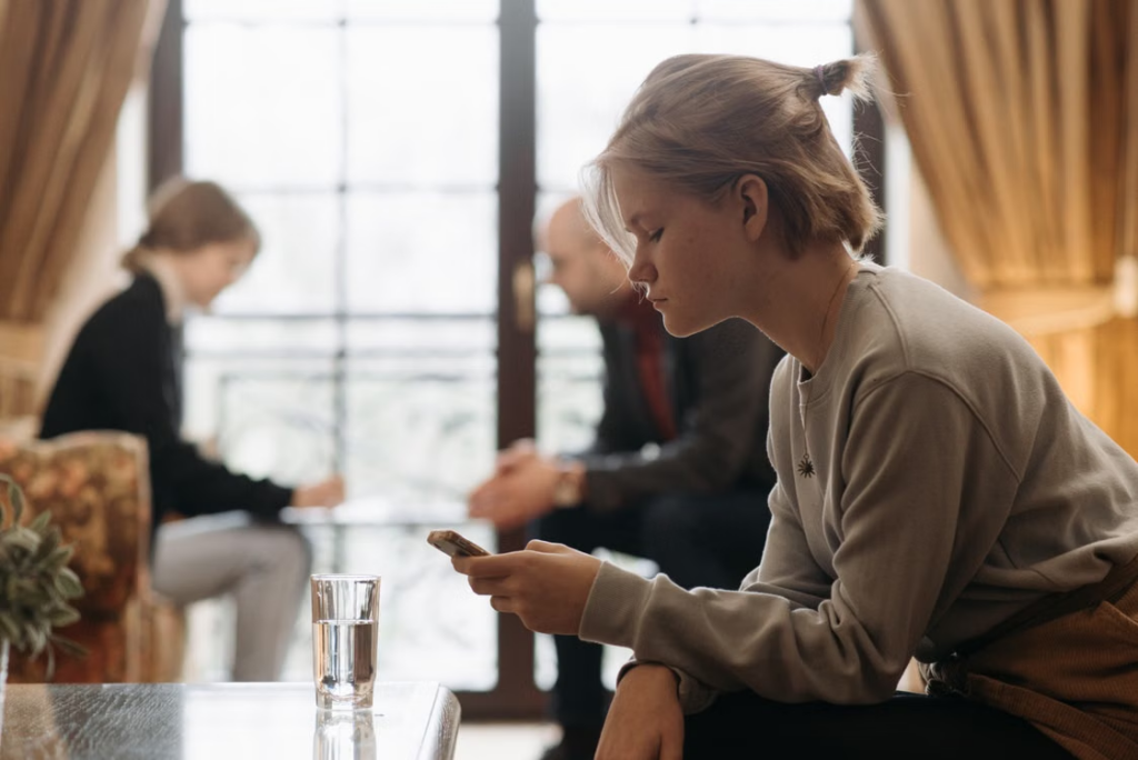 A teen using their phone next to adults 