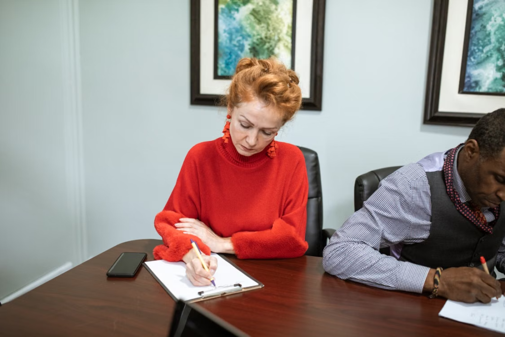 Two support workers reviewing documentation and taking notes during a quality assurance meeting.