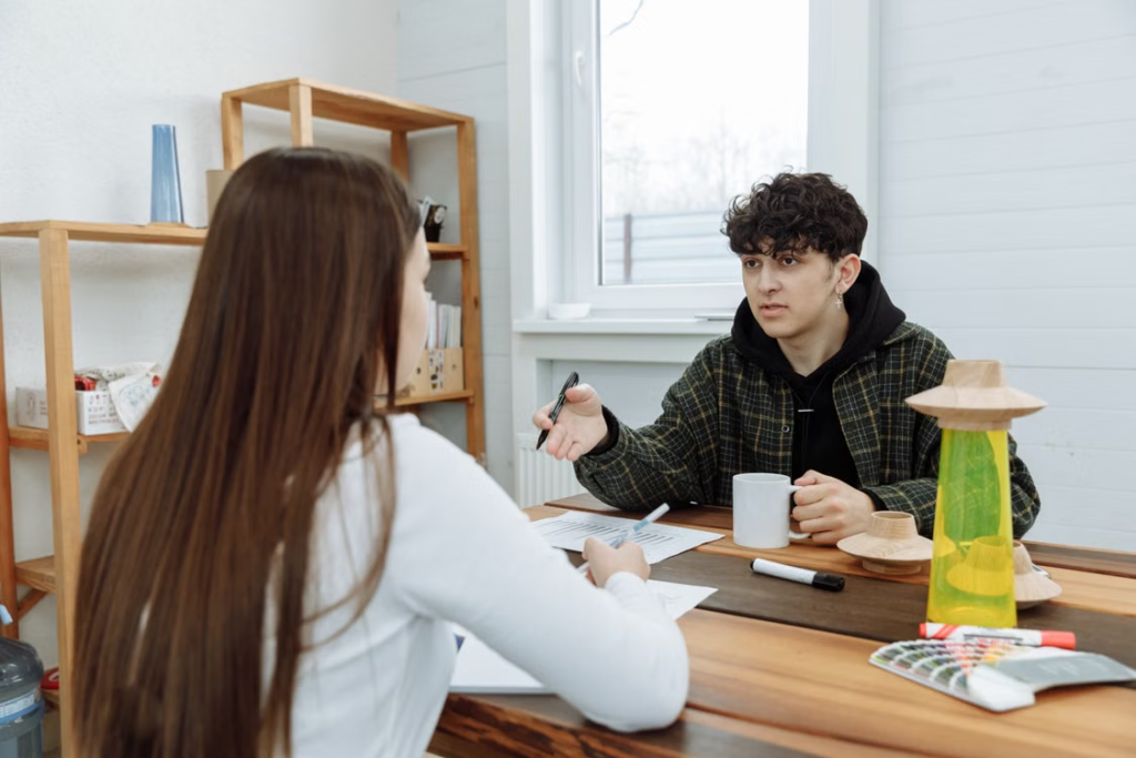 A support worker having a one-to-one check-in conversation with a young person at a table.