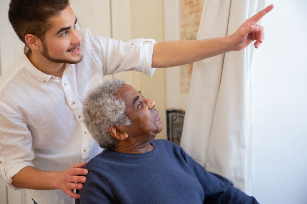 A support worker pointing something out to a smiling resident by a window.