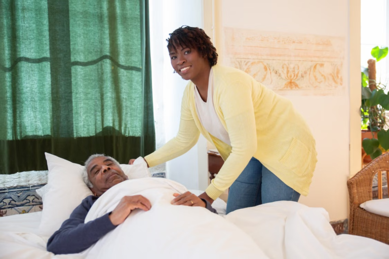 A support worker smiling while attending to a resident resting in bed.