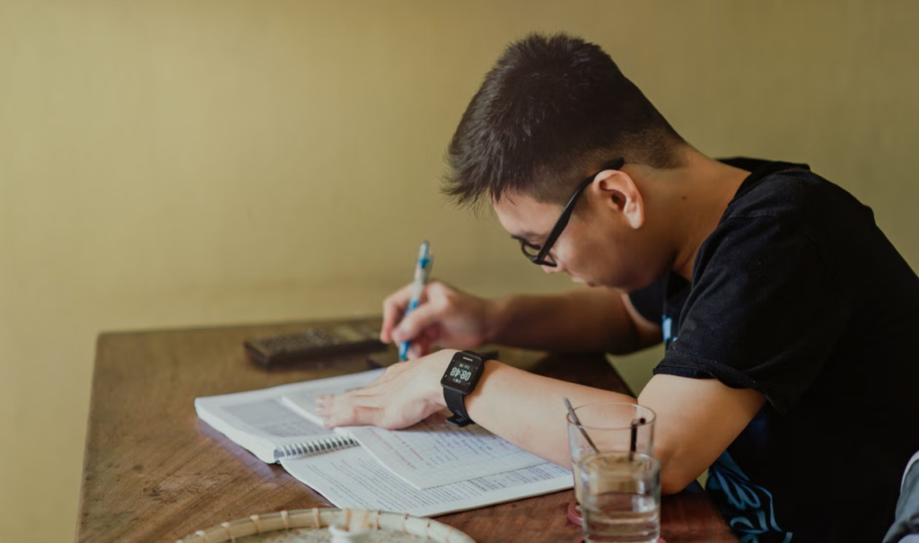A young man concentrating on studying at his desk, taking notes.