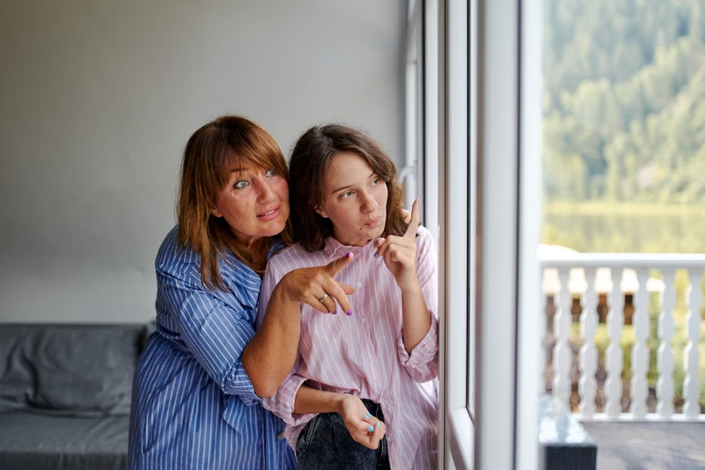 two women standing and looking out a window.